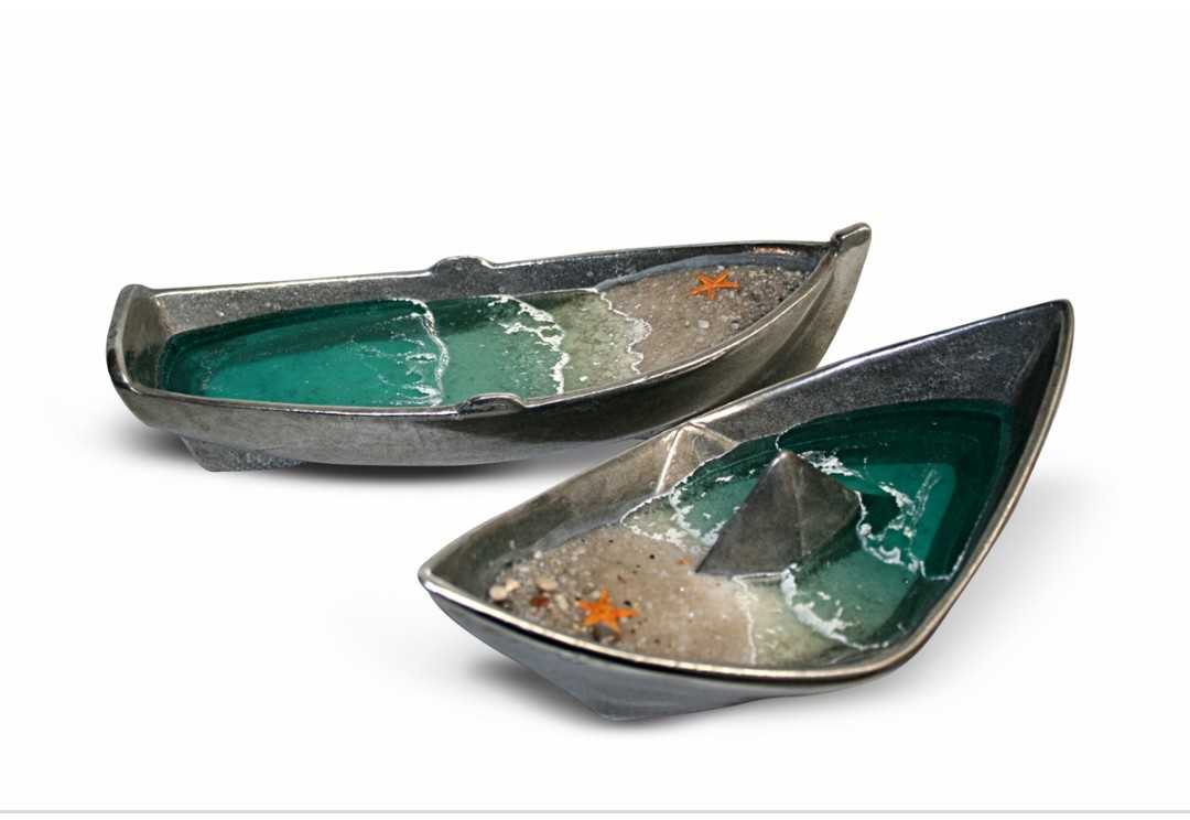 Stelios Gavalas sculpture from aluminium boats with pebbles and sea.